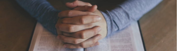 folded hands praying over a bible