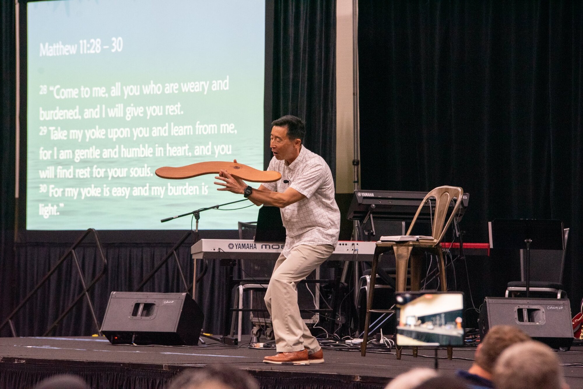 Image of an Asian man speaking on stage with a wooden object in his hands