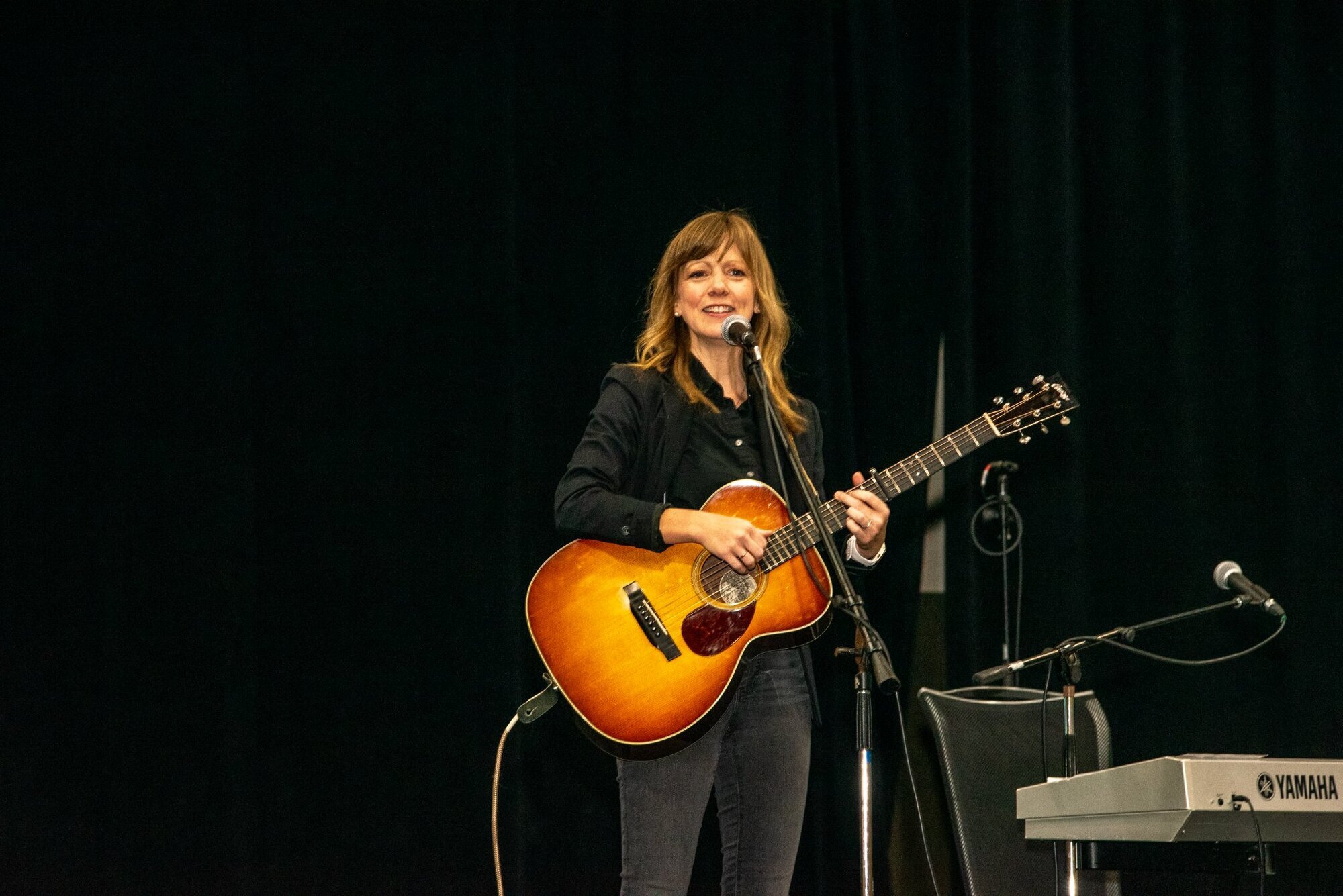 a white women singing into a microphone while playing guitar